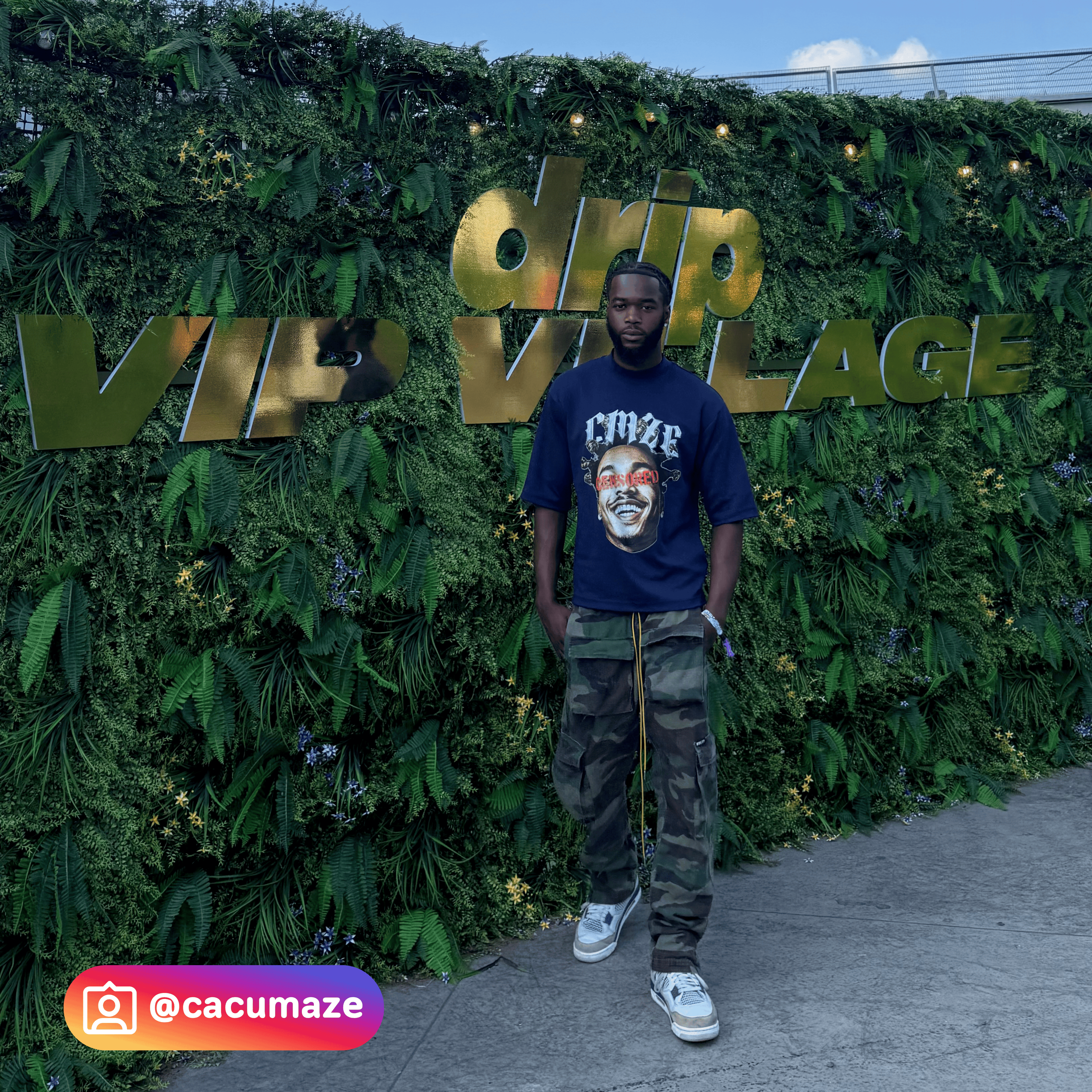 Person standing in front of a 'VIP Village' sign at festival with greenery.